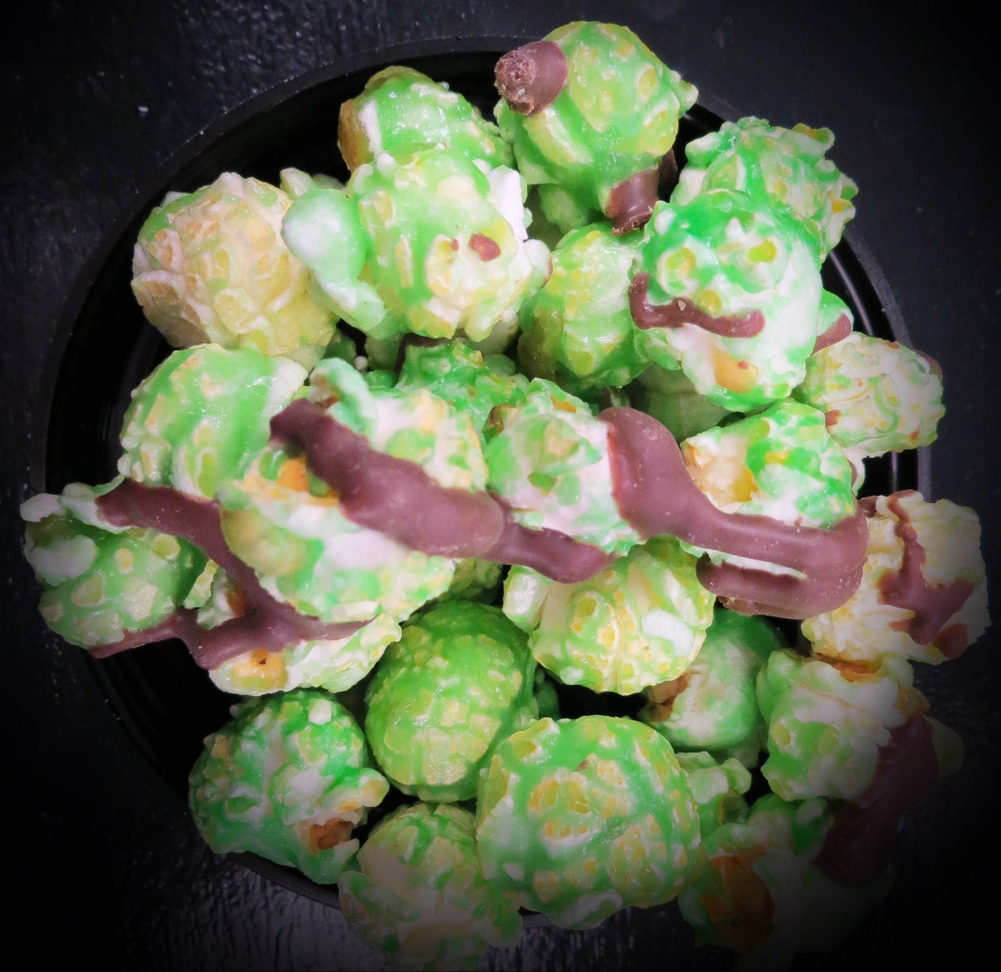 Mint chocolate chip popcorn with chocolate drizzle on a black background.