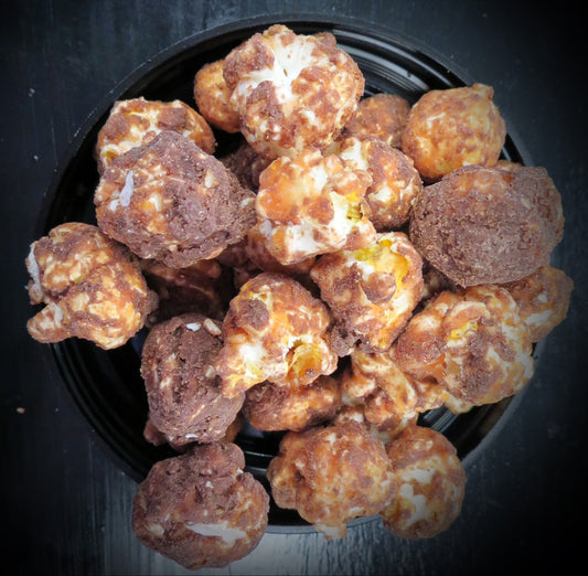 Chocolate peanut butter popcorn coated in creamy chocolate over black background.