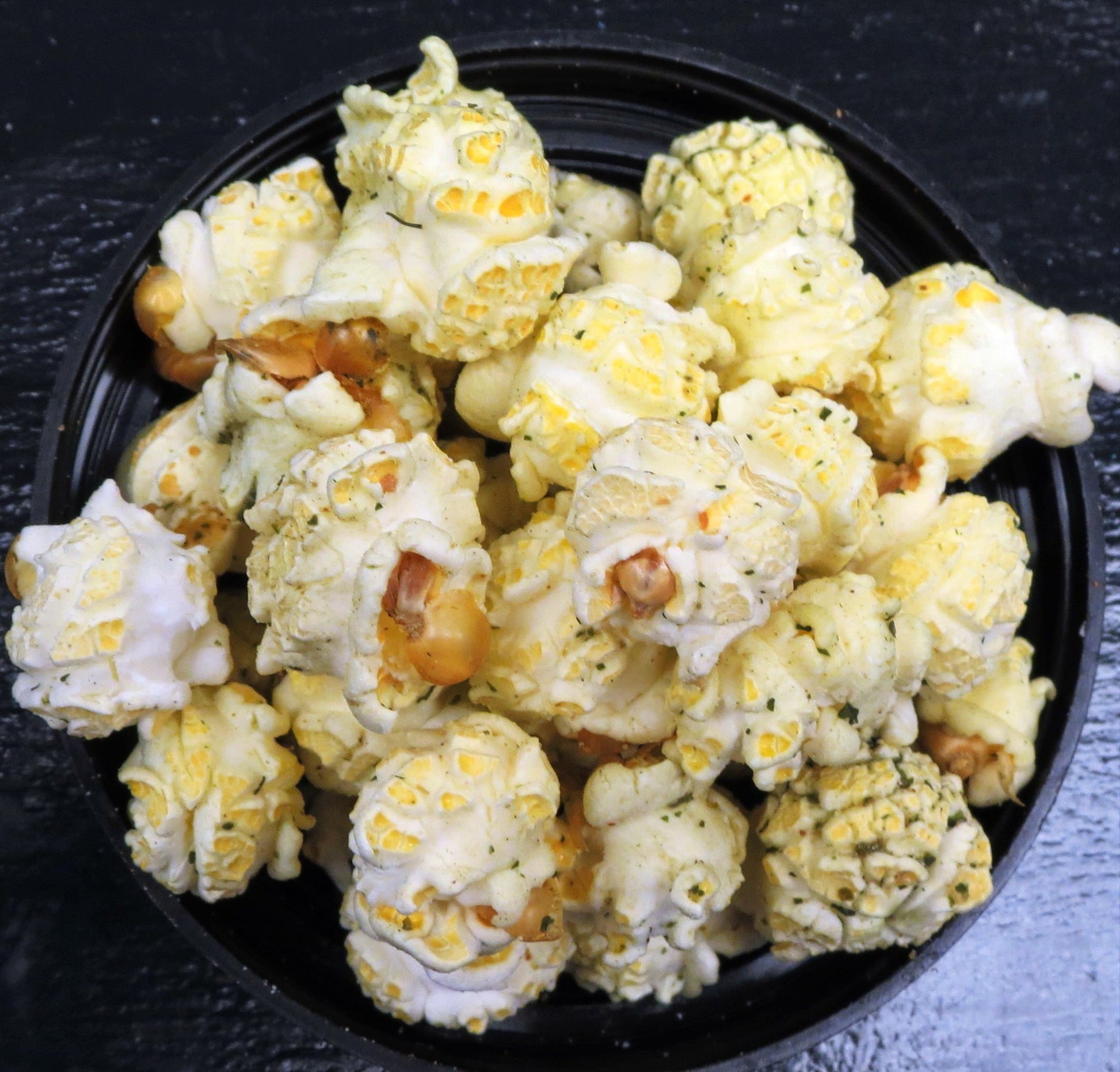 Dill-flavored popcorn in a black bowl, highlighted with dill weed seasoning.