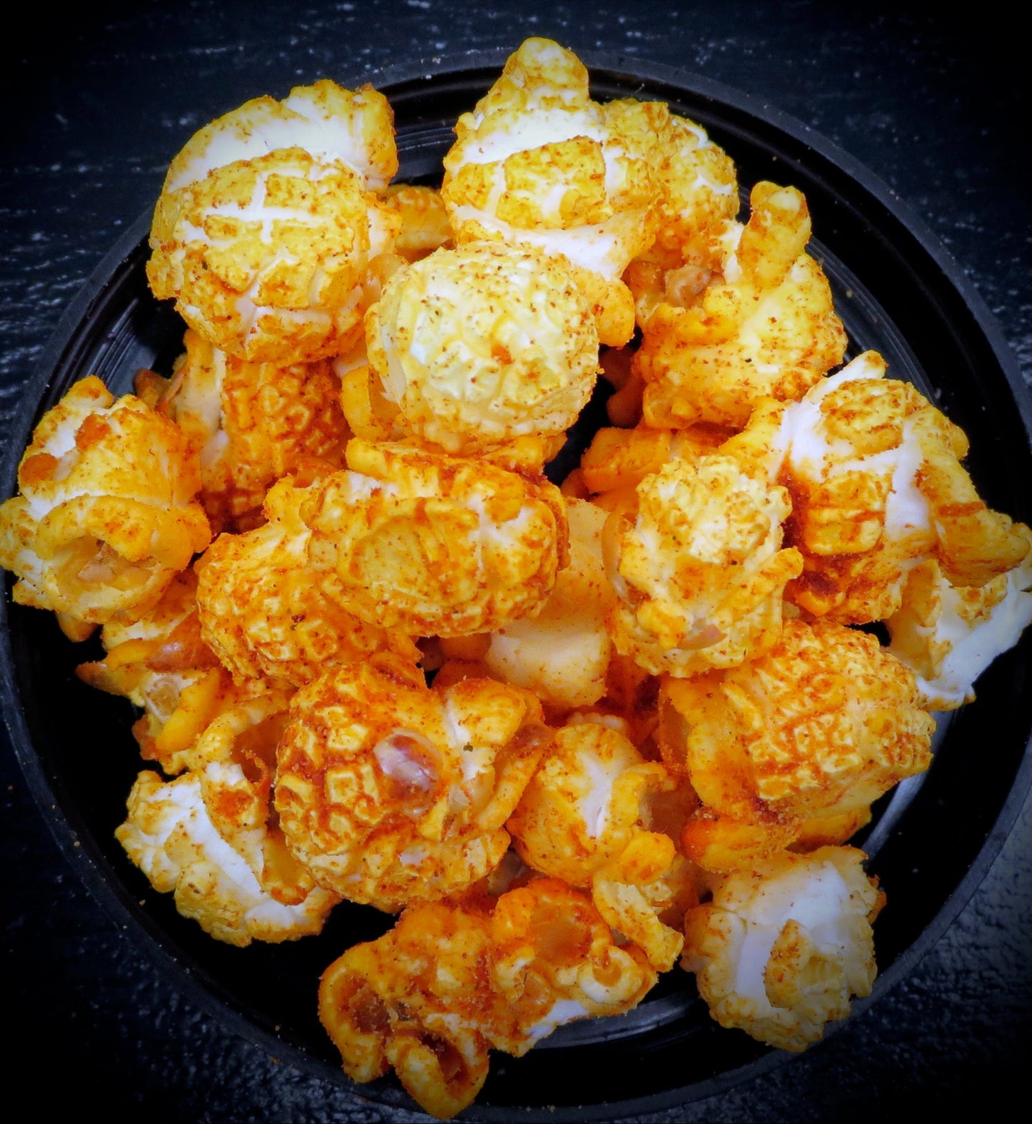 Cheese and pizza sauce flavored popcorn in a black bowl.