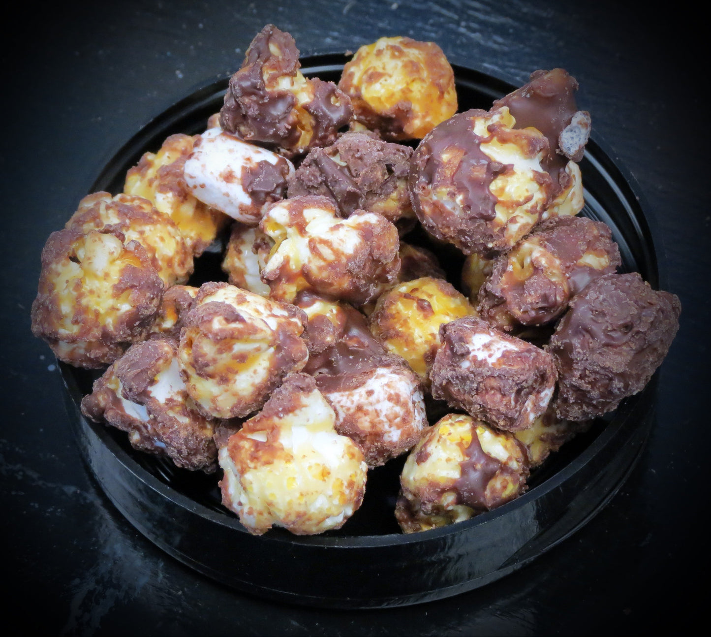 Yummy marshmallow flavored popcorn with milk chocolate, mini marshmallows, and graham crackers in a black bowl